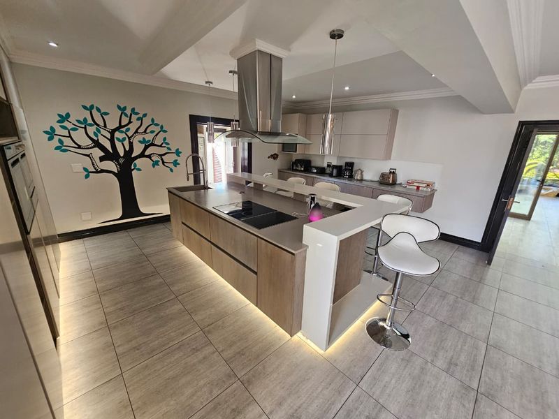 Modern kitchen featuring a large central island with integrated hob, stainless steel extractor fan, sleek cabinetry, and ambient under-cabinet lighting.