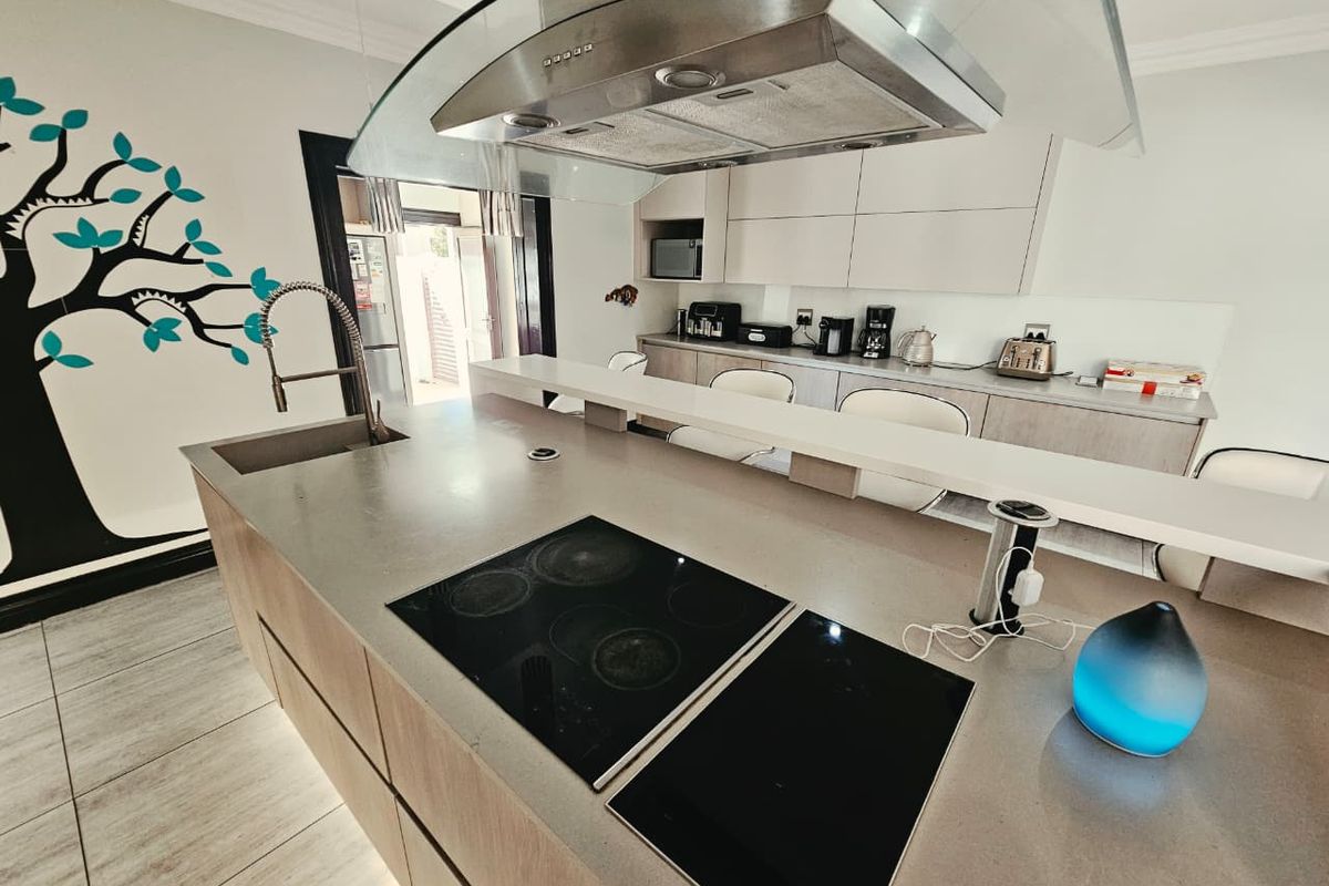 Modern kitchen featuring a large island with an integrated electric hob, sleek cabinetry, and a contemporary glass extractor hood.