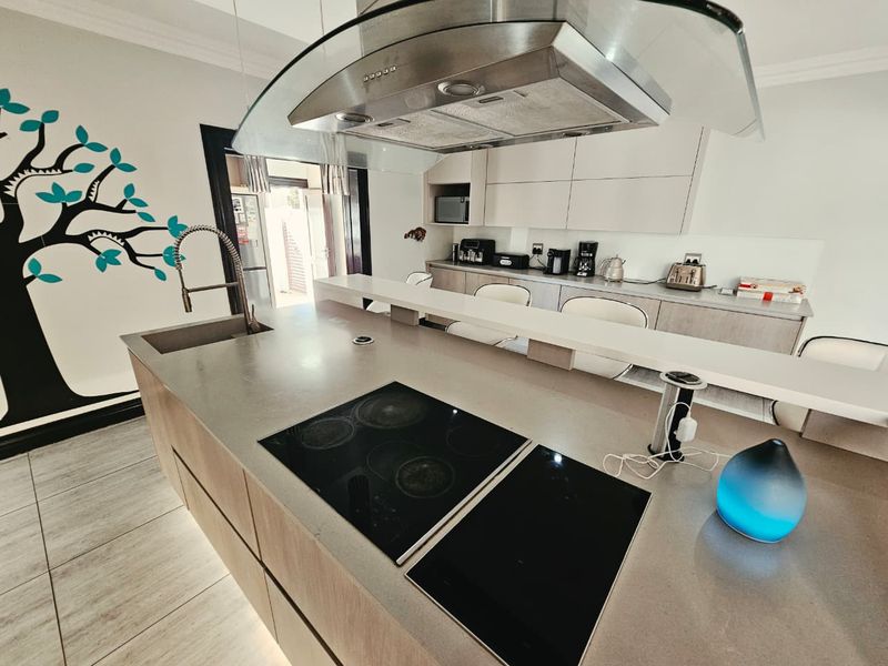 Modern kitchen featuring a large island with an integrated electric hob, sleek cabinetry, and a contemporary glass extractor hood.