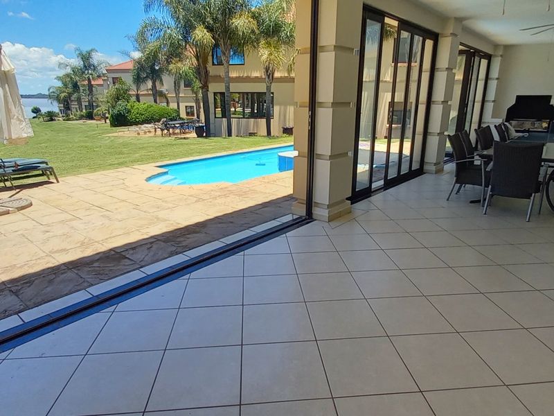 Spacious covered patio featuring tiled flooring and large sliding doors, seamlessly connecting to the outdoor pool area and garden with scenic water views.