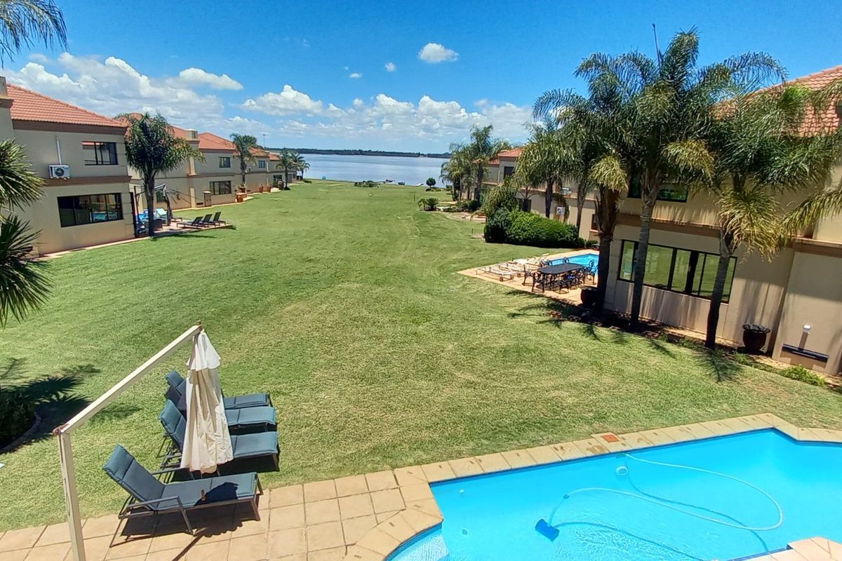 Elevated view overlooking a communal garden, swimming pool, and residential units with a scenic lake in the background.