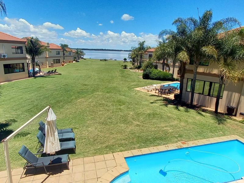 Elevated view overlooking a communal garden, swimming pool, and residential units with a scenic lake in the background.