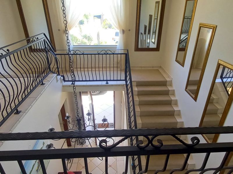 Spacious double-volume entrance hall featuring a wrought iron balustrade, tiled flooring, and a grand staircase leading to the upper level.