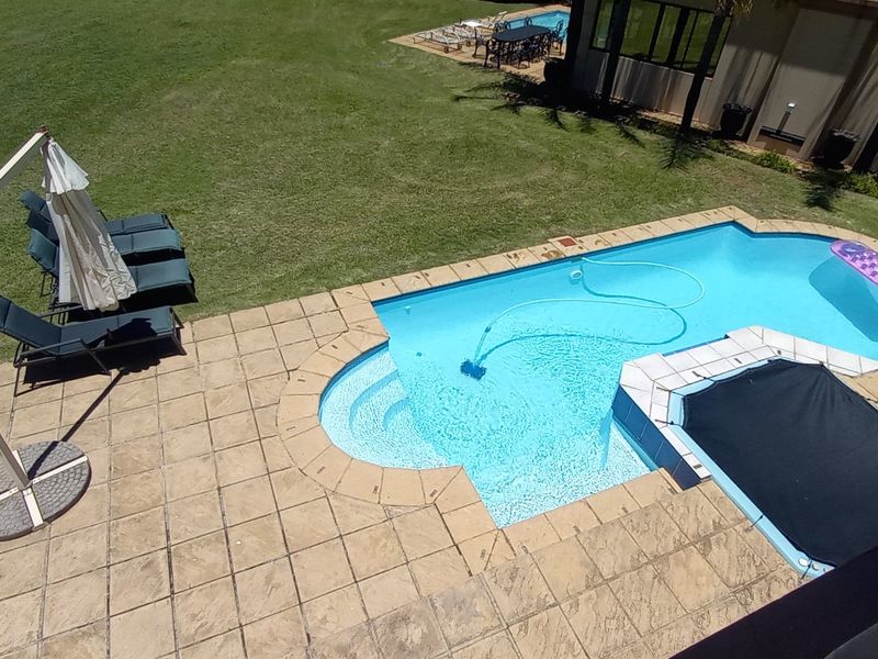 An elevated view of a swimming pool with a paved deck and surrounding lawn area, featuring a pool cover and integrated steps.