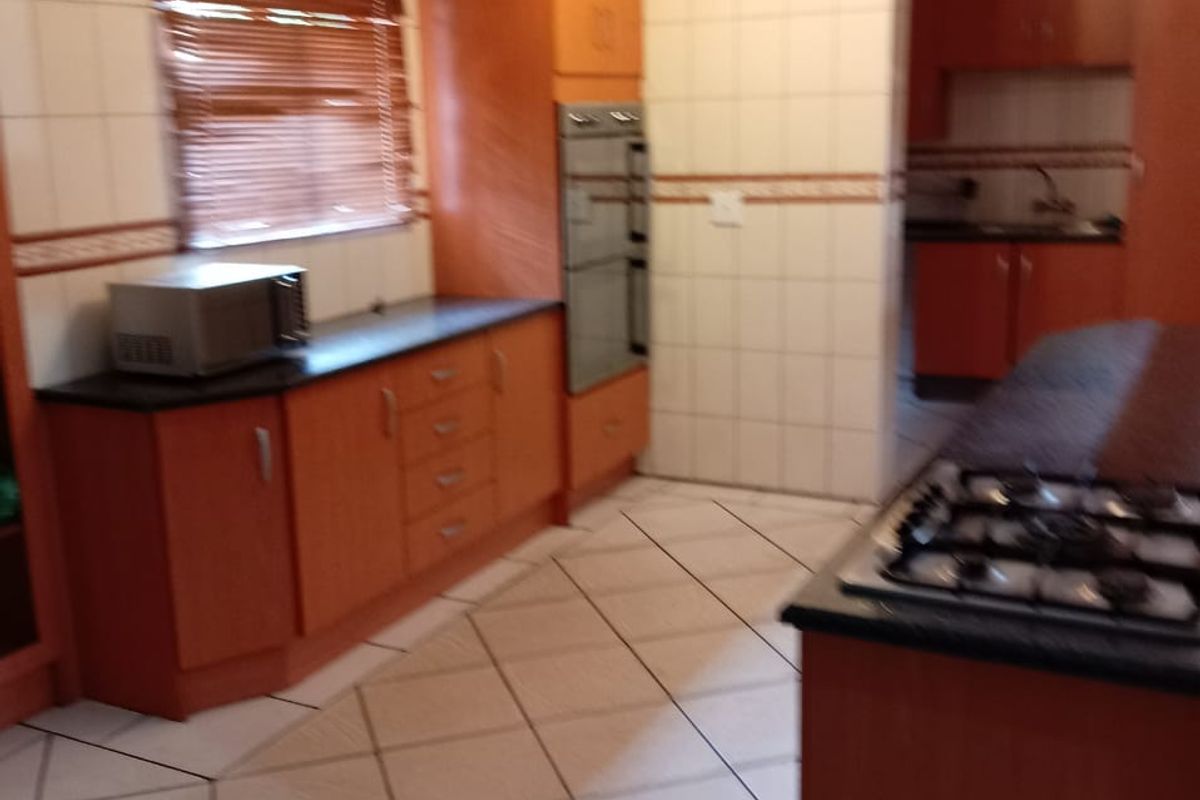 A functional kitchen featuring wooden cabinetry, built-in oven, gas hob, and tiled finishes, with an adjacent scullery area visible.