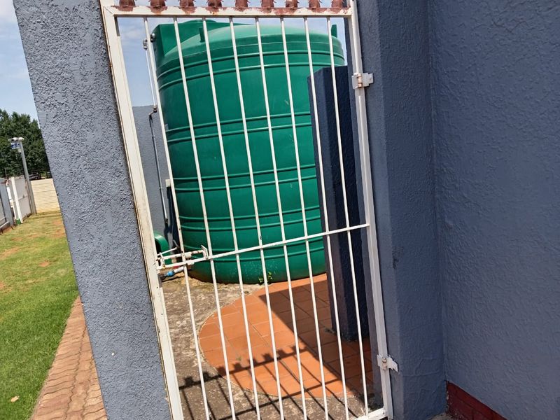 A utility area featuring a large green water storage tank secured behind a metal gate with tiled flooring.