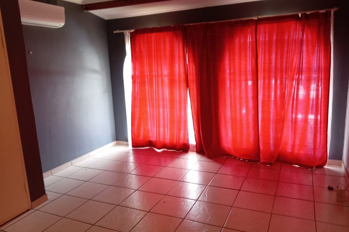 An empty living room featuring tiled flooring and a wall-mounted split-system air conditioner, providing a blank canvas for interior design.