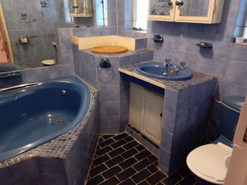 A dated bathroom featuring a built-in corner bathtub, tiled vanity with integrated basin, and toilet, requiring modernization of finishes and fixtures.