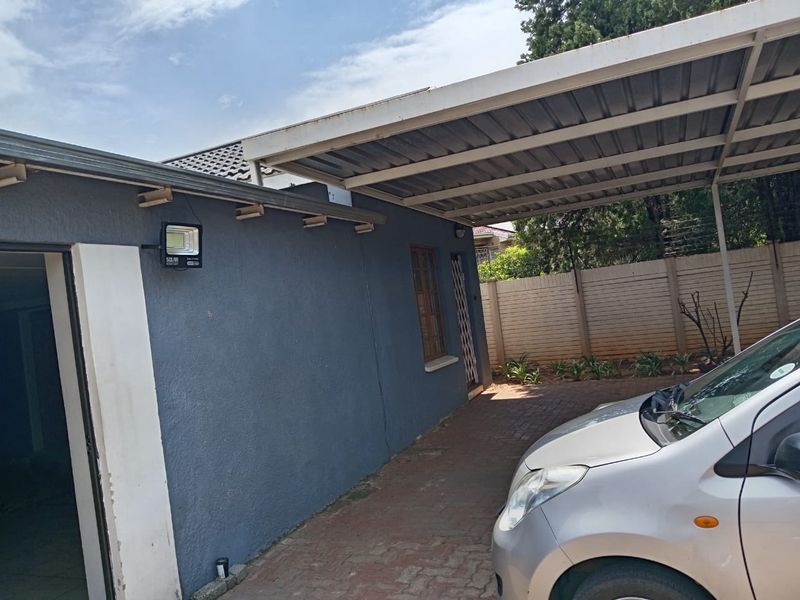Exterior view of the property featuring a covered carport, paved driveway, and perimeter walling with a mounted solar security light.