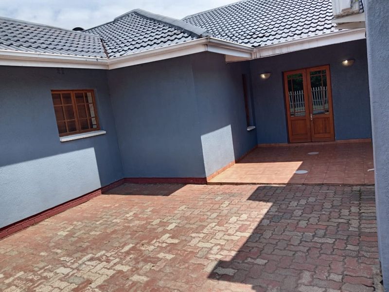 A well-maintained rear courtyard featuring paved flooring, a tiled roof, and double wooden entrance doors leading into the home.