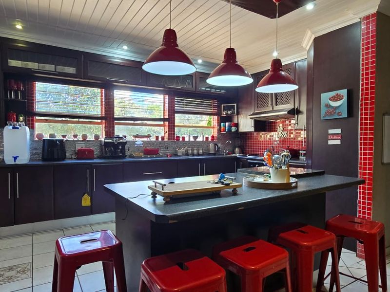 Spacious kitchen featuring dark cabinetry, a central island with seating, red tiled backsplash, and modern pendant lighting, offering a functional and distinct design.