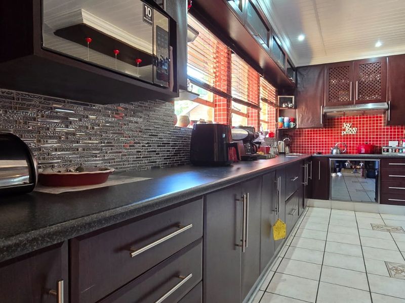 A well-maintained kitchen featuring dark wood cabinetry, contrasting tiled backsplashes, built-in appliances, and durable tiled flooring.