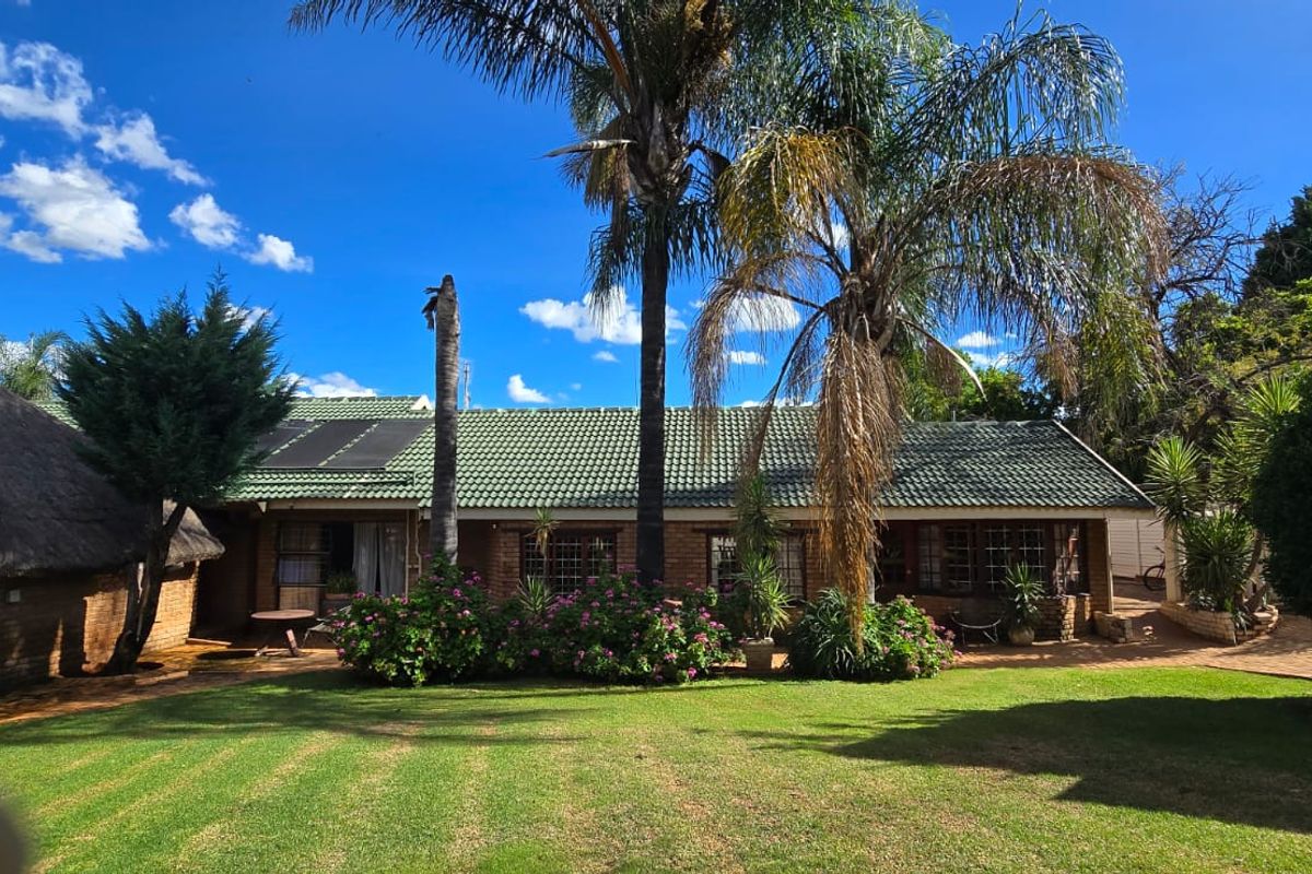 A spacious rear garden featuring a well-maintained lawn, paved patio area, and a combination of brick and thatched roof structures.
