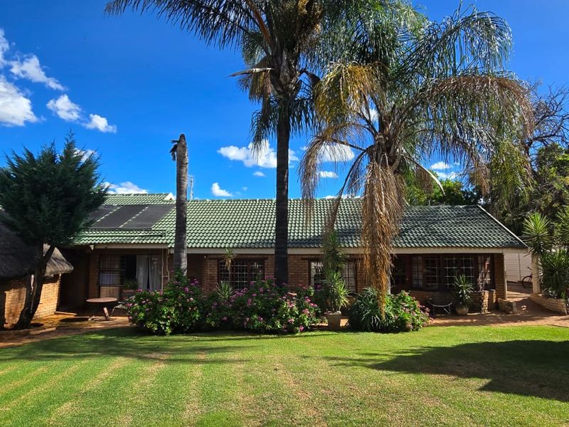 A spacious rear garden featuring a well-maintained lawn, paved patio area, and a combination of brick and thatched roof structures.