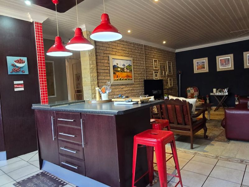 Spacious open-plan living area featuring a kitchen island, tiled flooring, and an exposed brick feature wall, seamlessly connecting the kitchen and lounge space.