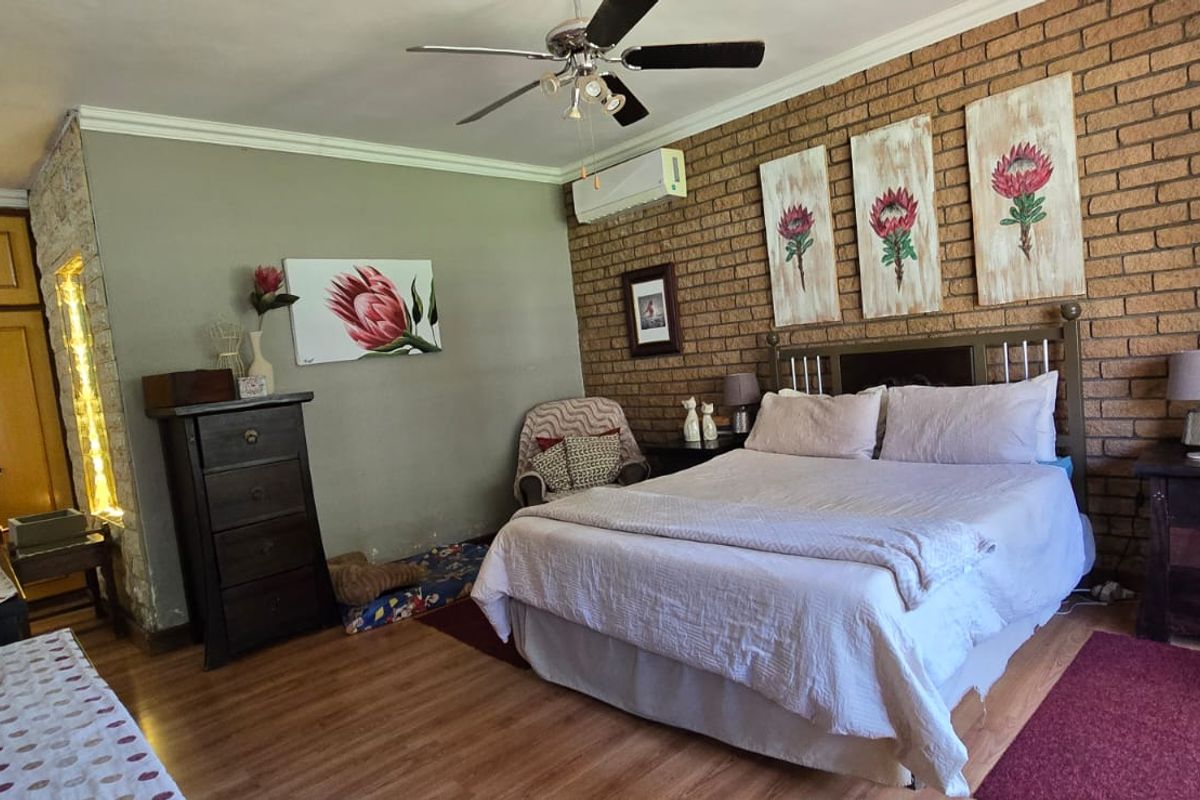 A spacious bedroom featuring an exposed brick feature wall, laminate flooring, built-in cupboards, and a ceiling fan with an integrated air conditioning unit.