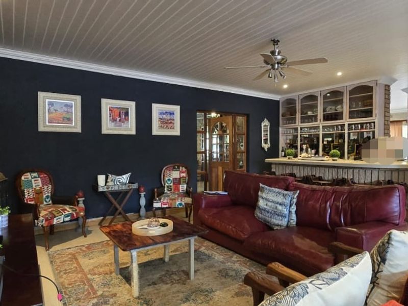 Spacious open-plan living area featuring a brick accent wall, built-in bar with display cabinetry, and a classic tongue and groove ceiling.