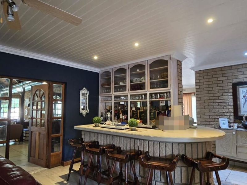 A dedicated bar area featuring a built-in counter, custom cabinetry, exposed brick feature wall, and timber-framed glass doors leading to adjacent living spaces.