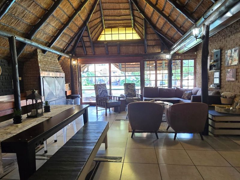Spacious living area featuring a high thatched roof with exposed timber beams, exposed brick walls, a built-in fireplace, and large sliding doors to the exterior.
