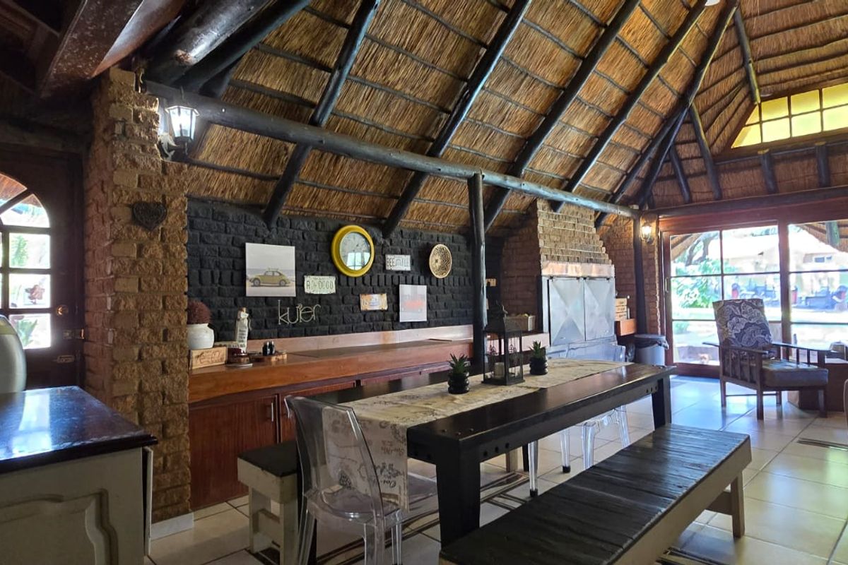 Spacious living area featuring a high thatched roof with exposed timber beams, an exposed brick feature wall, and a built-in fireplace.