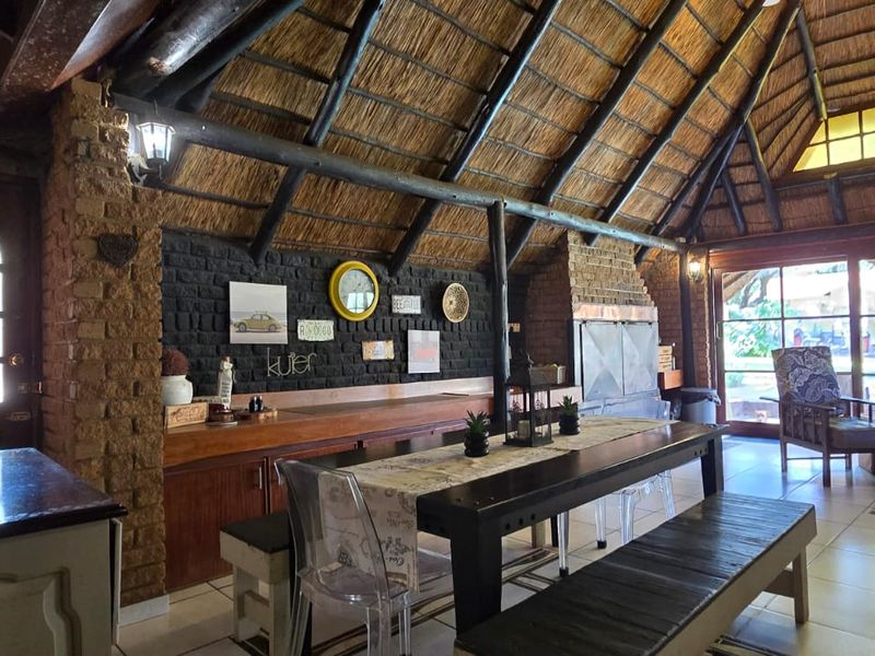 Spacious living area featuring a high thatched roof with exposed timber beams, an exposed brick feature wall, and a built-in fireplace.