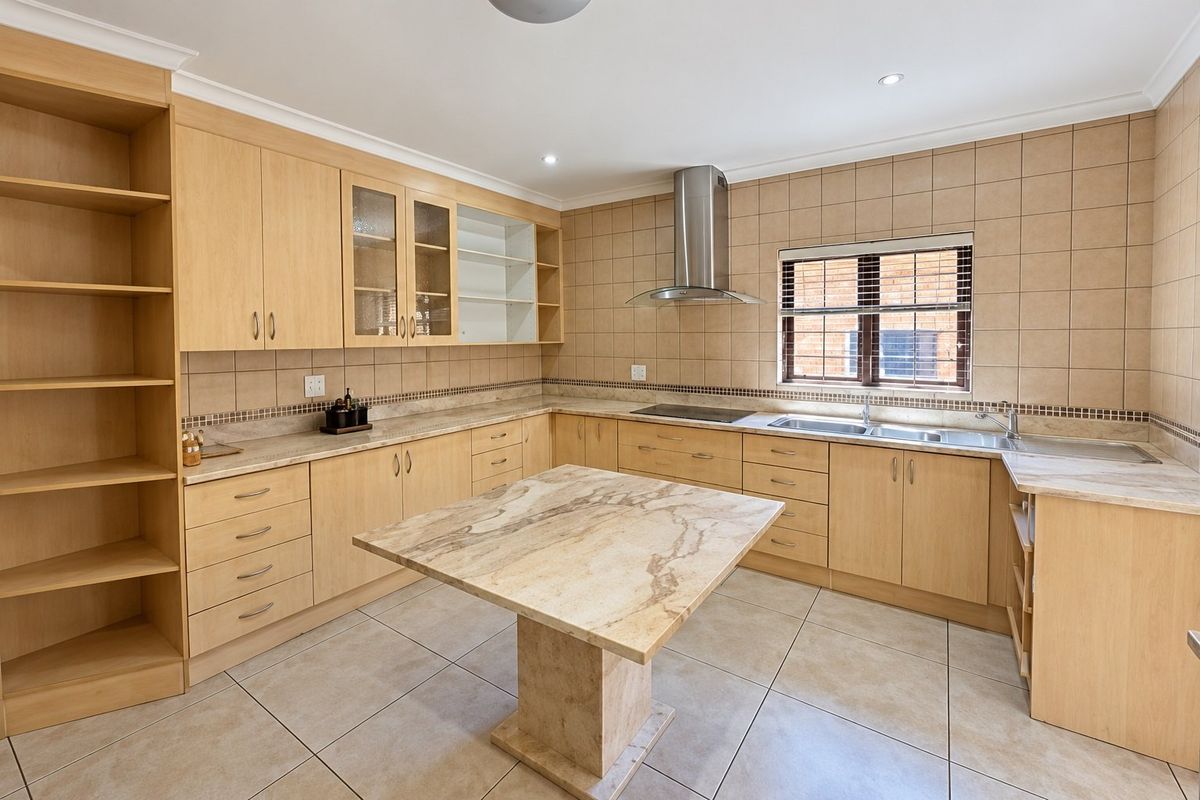 Spacious kitchen featuring light wood cabinetry, stone countertops, a central island, and integrated stainless steel appliances with neutral tiled finishes.