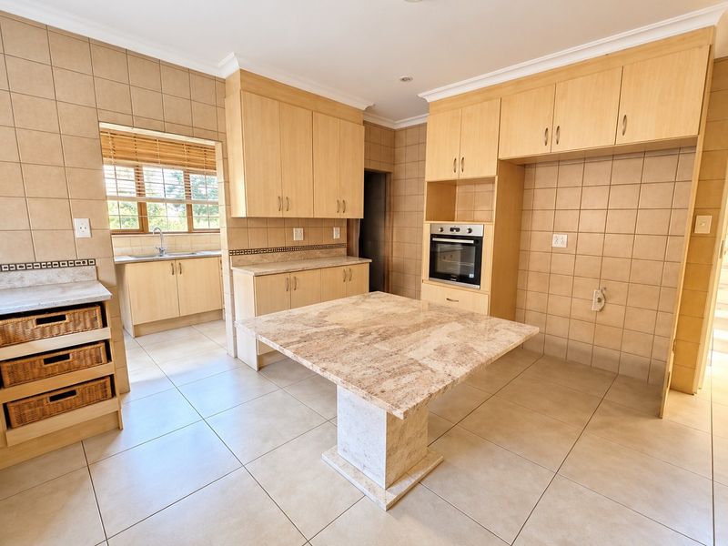 Spacious kitchen featuring light wood cabinetry, stone countertops, a central island, built-in oven, and tiled finishes throughout.