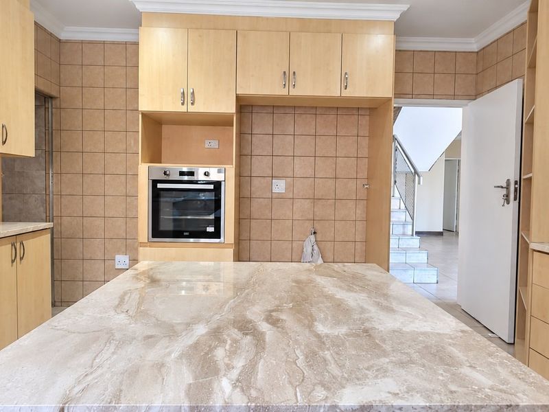 A functional kitchen featuring light wood cabinetry, stone countertops, and a built-in oven, offering a clean and neutral space ready for personalization.