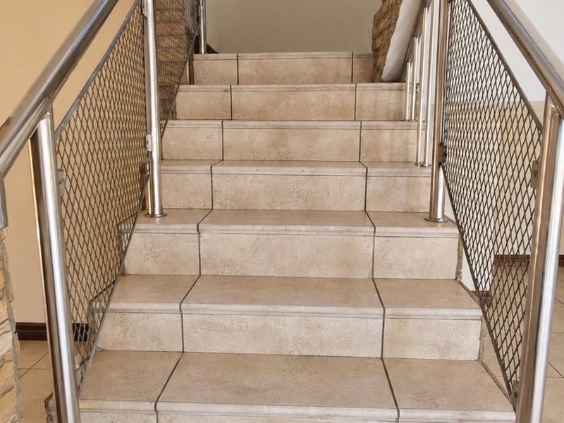 A well-maintained staircase featuring neutral ceramic tiling, modern stainless steel balustrades with wire mesh infill, and a decorative stone-clad feature wall.