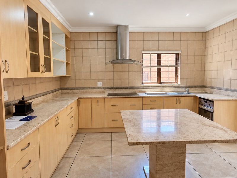 Spacious kitchen featuring light wood cabinetry, granite countertops, a central island, built-in oven, and stainless steel extractor fan with neutral tiled finishes.