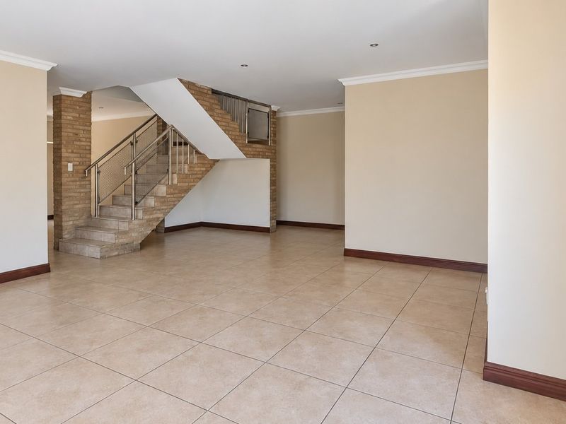 Spacious, open-plan living area featuring neutral tiled flooring, a prominent brick staircase with metal balustrade, and a recessed wall niche.