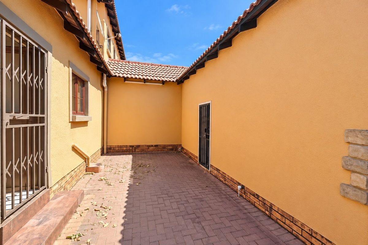 A clean, paved rear courtyard area featuring yellow exterior walls, a tiled roof, and secure access gates.