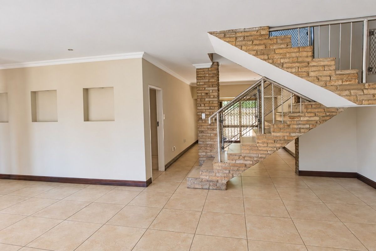 Spacious open-plan living area featuring a distinctive brick staircase with metal balustrade, tiled flooring, and decorative recessed wall niches.