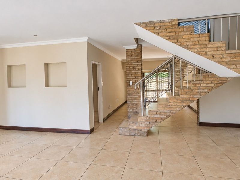 Spacious open-plan living area featuring a distinctive brick staircase with metal balustrade, tiled flooring, and decorative recessed wall niches.