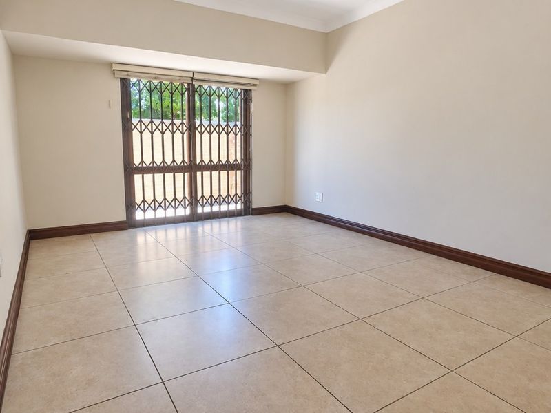 An empty living room featuring neutral tiled flooring, a stone feature wall, and a secure metal gate leading to the exterior.