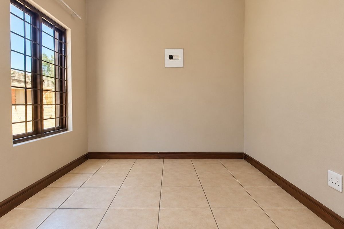 A clean, empty bedroom featuring neutral tiled flooring, secure window bars, and simple finishes, providing a versatile space ready for personalization.
