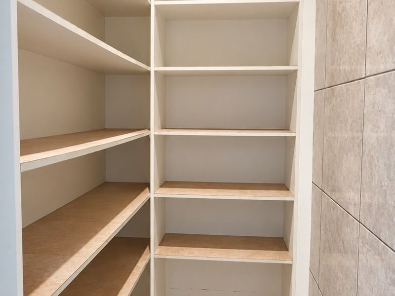 A clean, functional walk-in pantry or scullery area featuring extensive built-in shelving and durable tiled finishes.