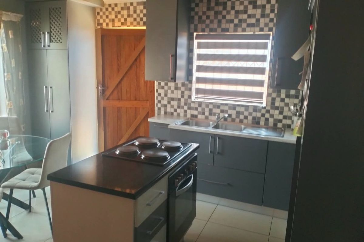 Modern kitchen featuring dark grey cabinetry, a central island with a built-in oven and hob, tiled splashback, and a double sink.