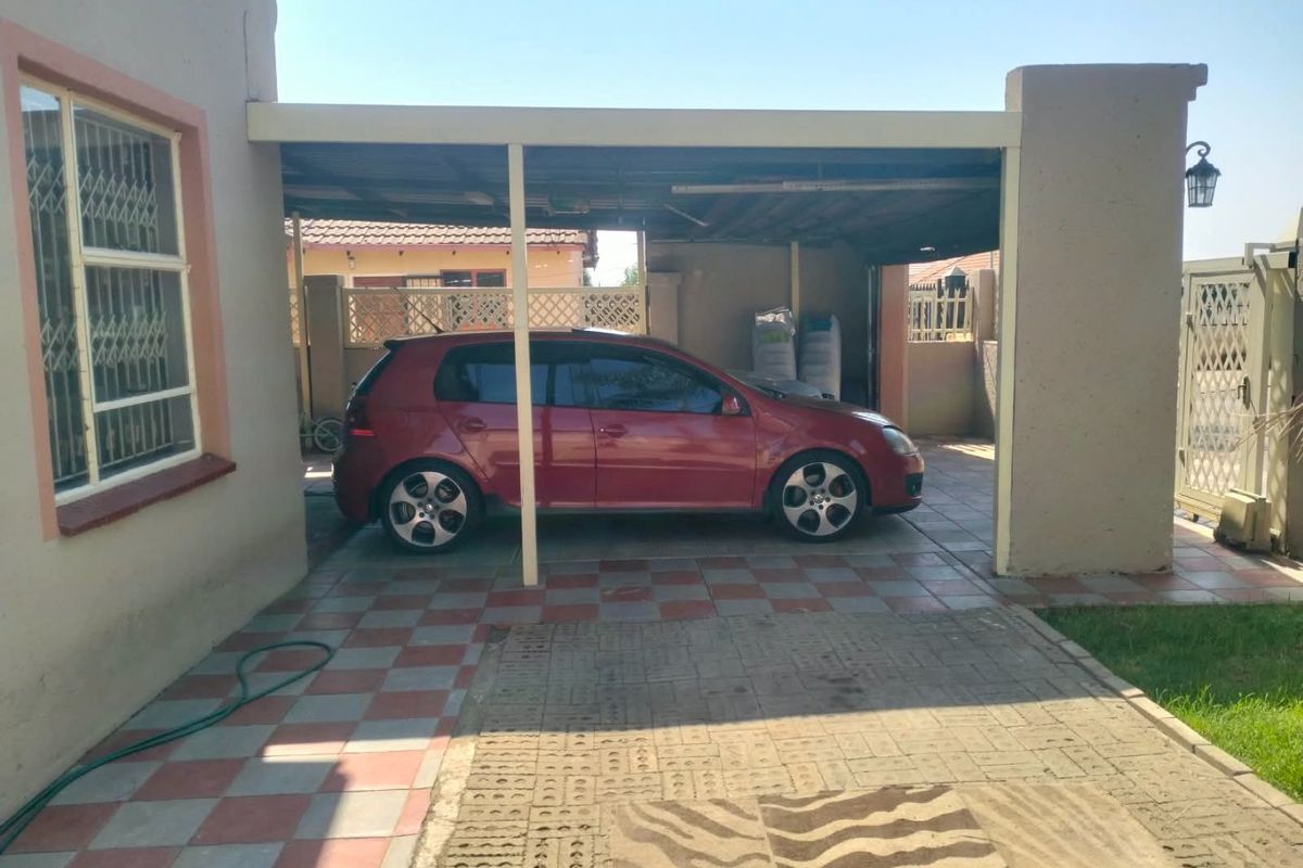 A paved rear courtyard area featuring a covered carport structure, tiled flooring, and secure perimeter fencing.