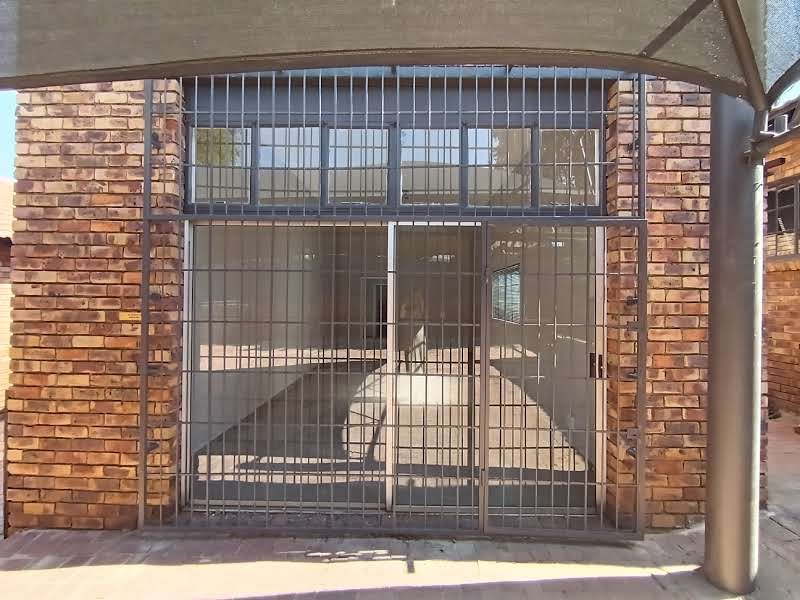 Commercial building entrance featuring a face brick facade, secure metal gate, and overhead shade sail protection.
