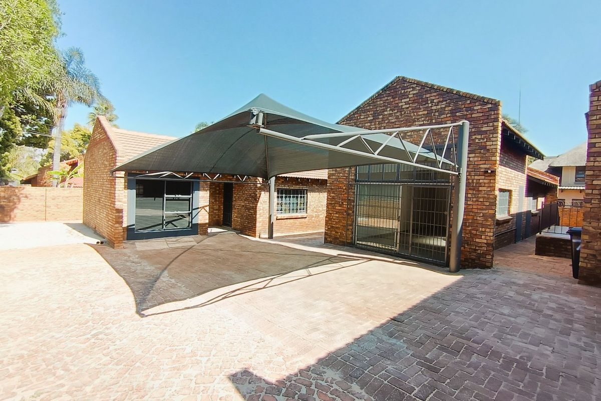 Rear exterior view of a commercial property featuring face brick construction, a paved courtyard area, and a large shade cloth carport structure.