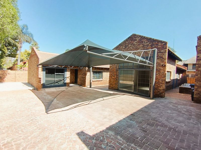 Rear exterior view of a commercial property featuring face brick construction, a paved courtyard area, and a large shade cloth carport structure.