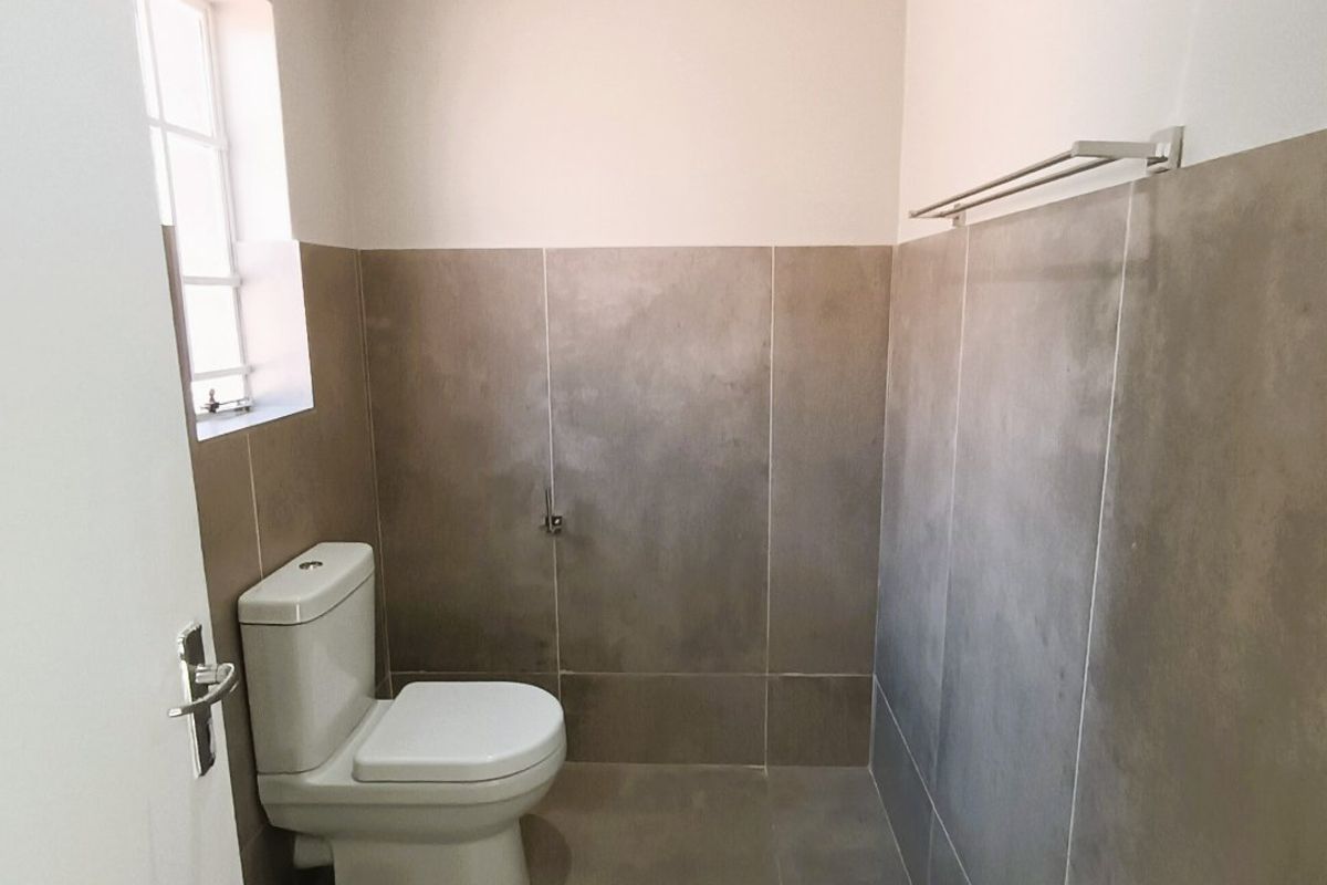 A clean, modern bathroom featuring neutral large-format wall and floor tiles, a white toilet, and a fitted towel rail.