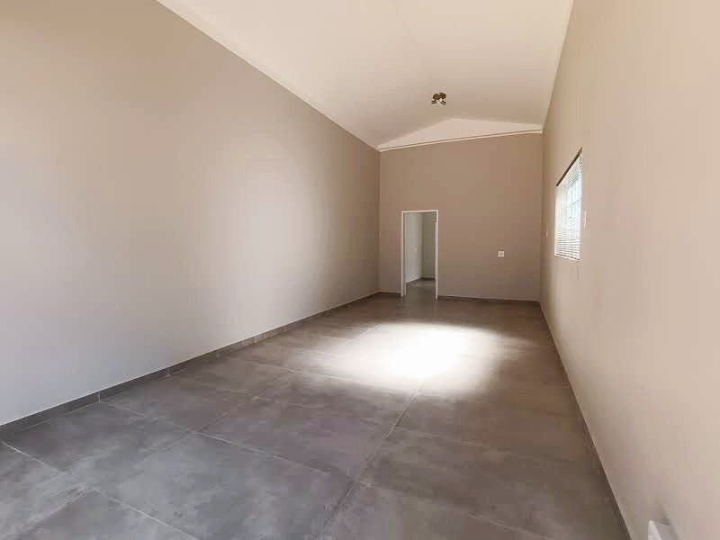 A spacious, empty commercial office area featuring vaulted ceilings, neutral wall finishes, and large format floor tiles with natural light.