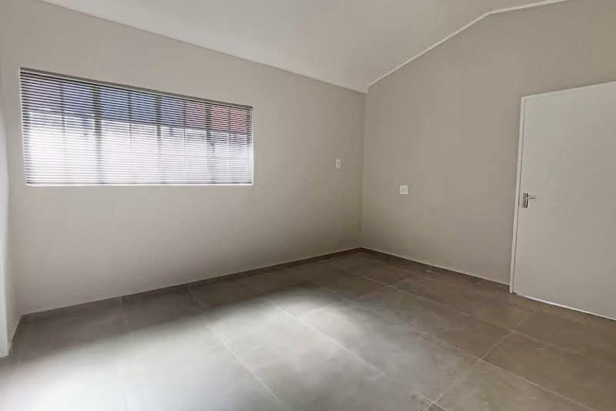 A clean, empty bedroom featuring neutral wall tones, large format floor tiles, and fitted venetian blinds, offering a versatile space ready for occupancy.