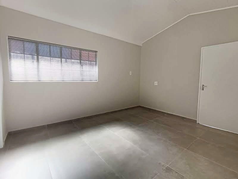 A clean, empty bedroom featuring neutral wall tones, large format floor tiles, and fitted venetian blinds, offering a versatile space ready for occupancy.