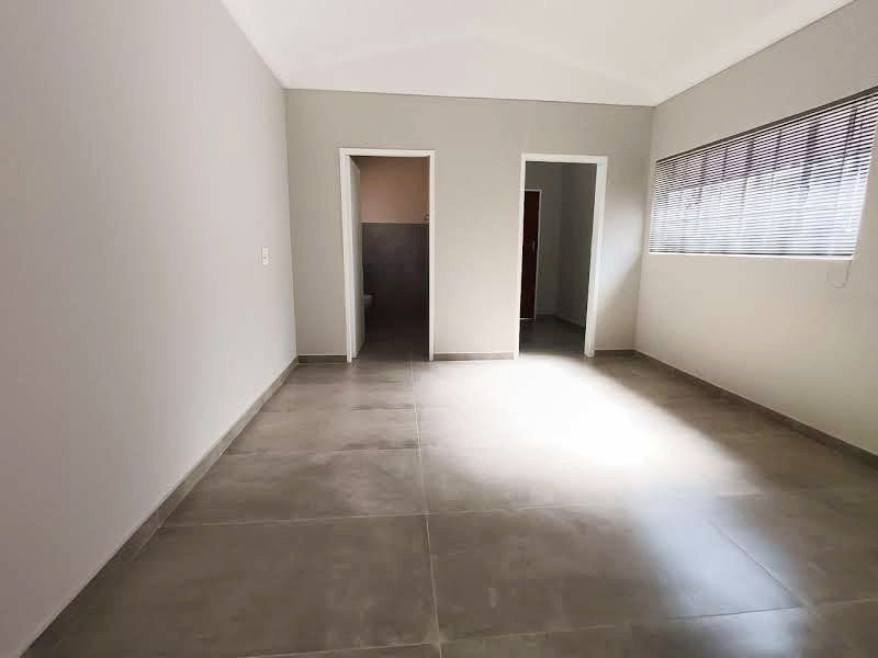 A bright, vacant office space featuring large format floor tiles, neutral wall finishes, and fitted venetian blinds, offering a clean and professional environment.