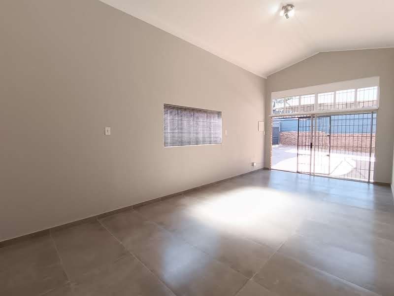 A spacious, empty living area featuring vaulted ceilings, large format floor tiles, and a sliding glass door with security gate leading to the exterior.