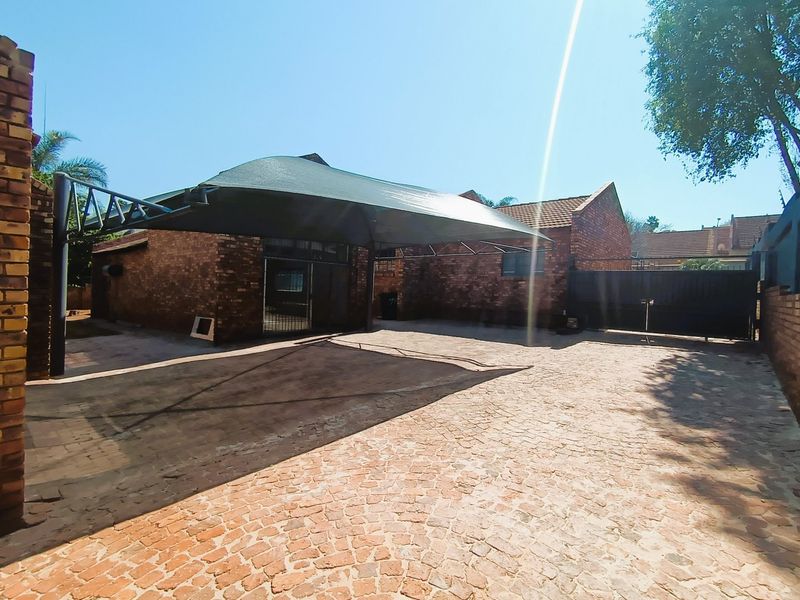 Exterior view of a commercial property featuring a paved driveway, face brick building facade, and a large shade cloth carport structure.