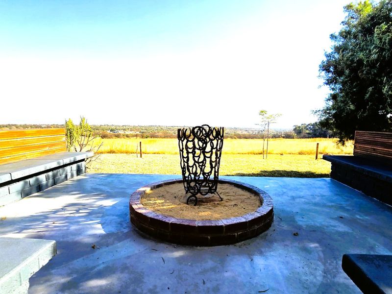 Outdoor patio area featuring a built-in brick fire pit, concrete flooring, and integrated bench seating with timber accents, overlooking a scenic landscape.